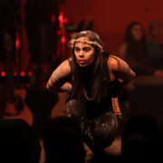 aboriginal woman wearing face paint is bending forward in a dance motion